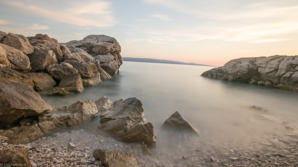 Skalista zatoka w Breli z jasnymi kamieniami i spokojną wodą w ciepłym świetle.