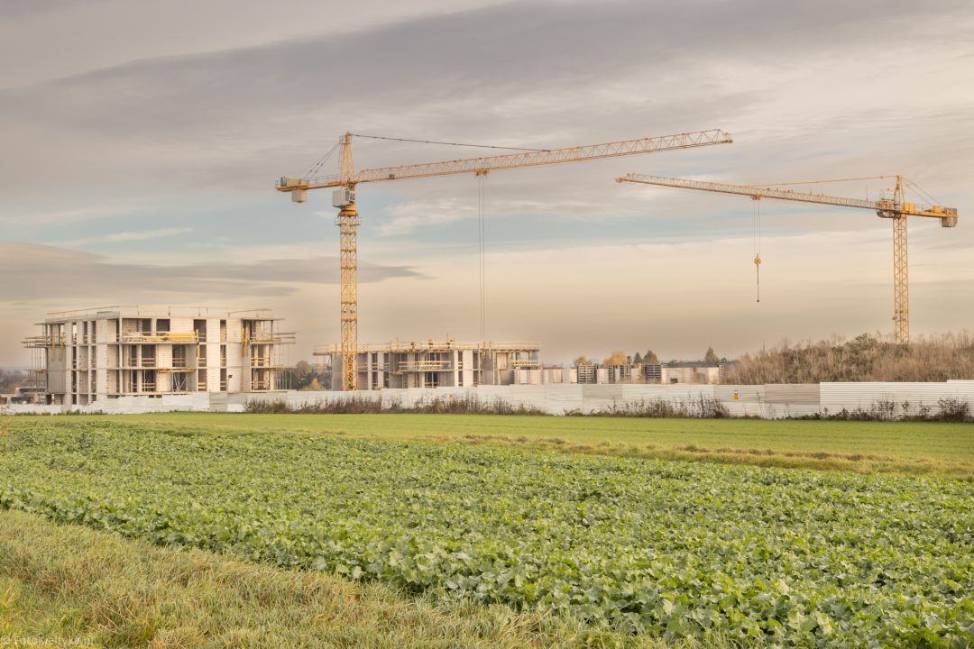 Żurawie wieżowe nad placem budowy osiedla mieszkaniowego na tle wieczornego nieba