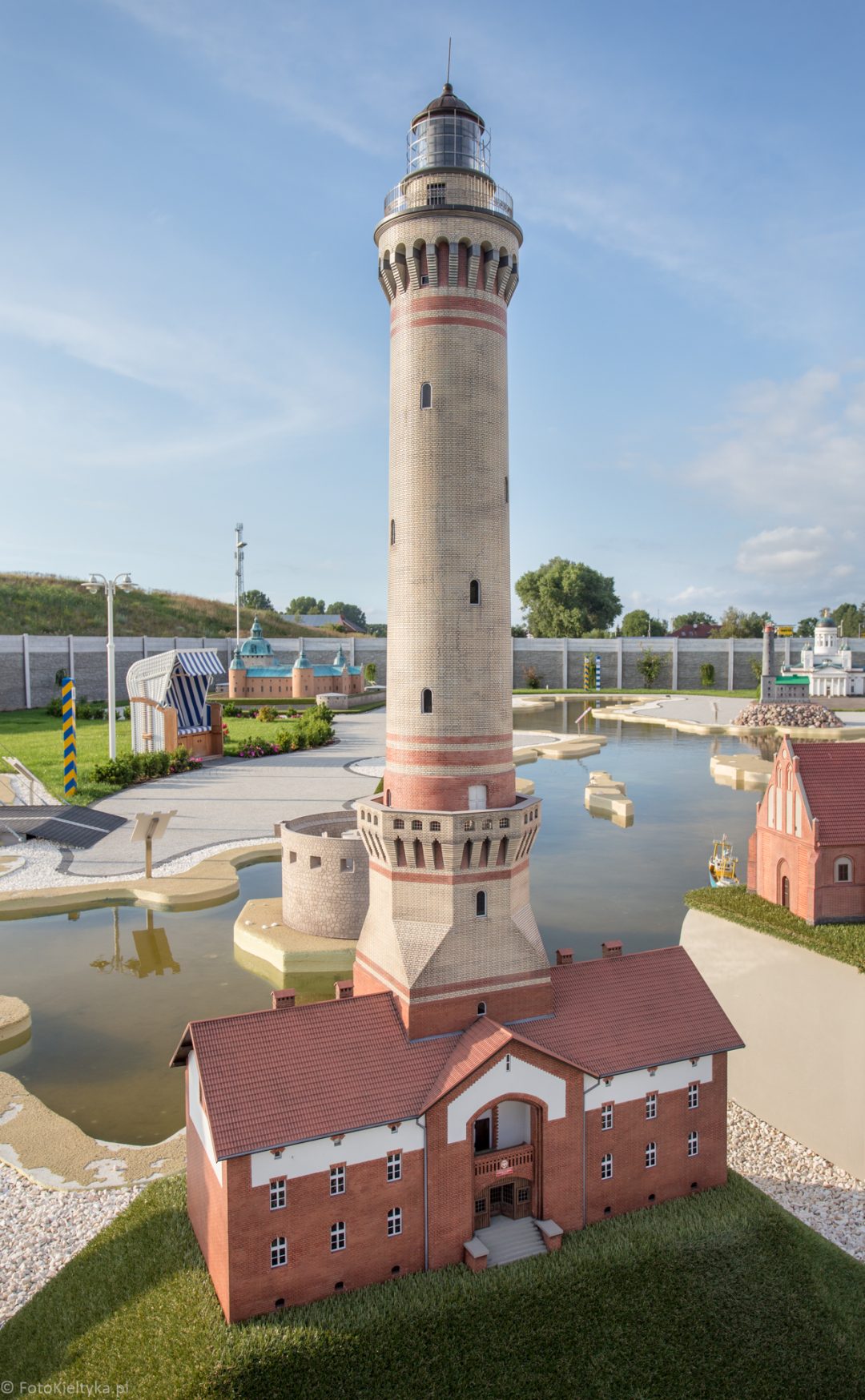 Wysoka cylindryczna wieża w parku miniatur, z innymi modelami w tle.